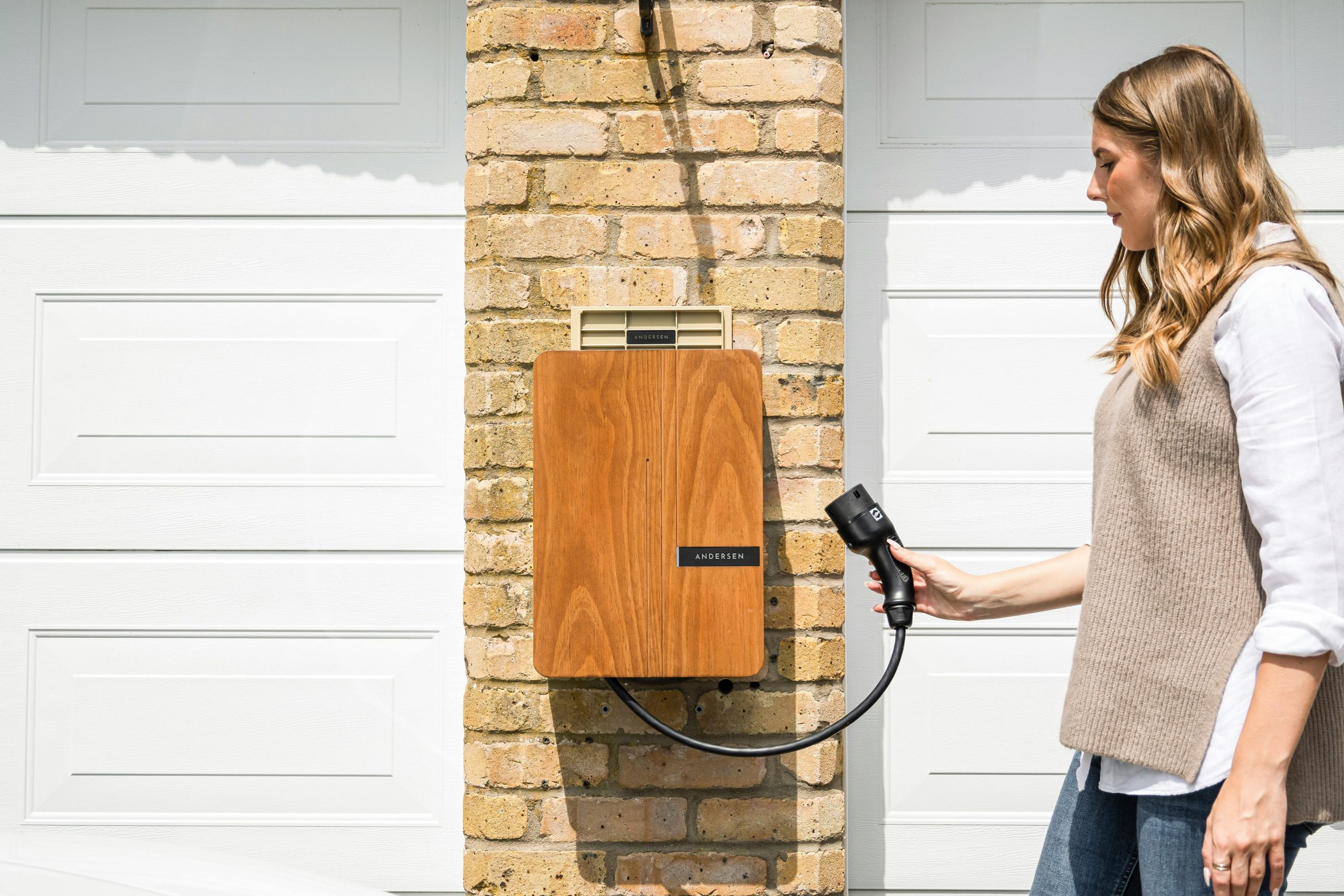 A woman uses a home electric vehicle charger mounted on a brick wall.